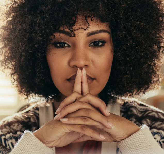 A black woman with afro hair covering her mouth with her hands.